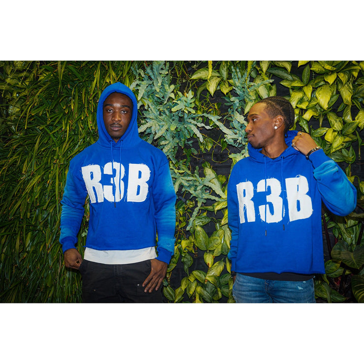 Two men wearing a blue crop hoodie with a design that shows &
