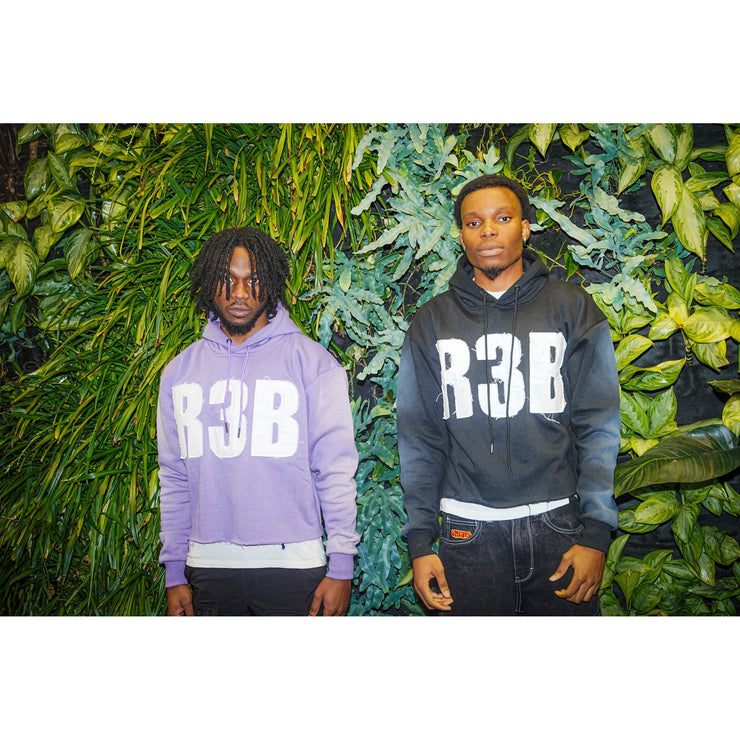 Two men wearing a lavender and black crop hoodie with a design that shows &